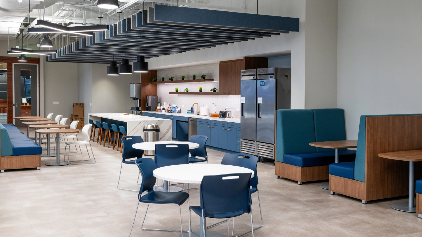 Office breakroom with booth seating, round bistro tables, and full kitchen with dual refrigerators