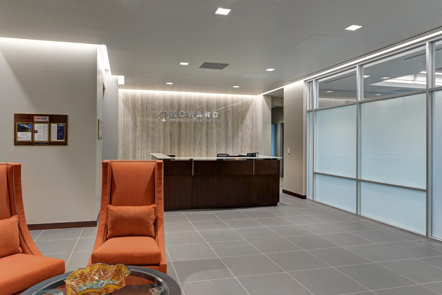 Howard Energy Partners office lobby with dark wood reception desk, backlit stone accent wall, and orange lounge chairs