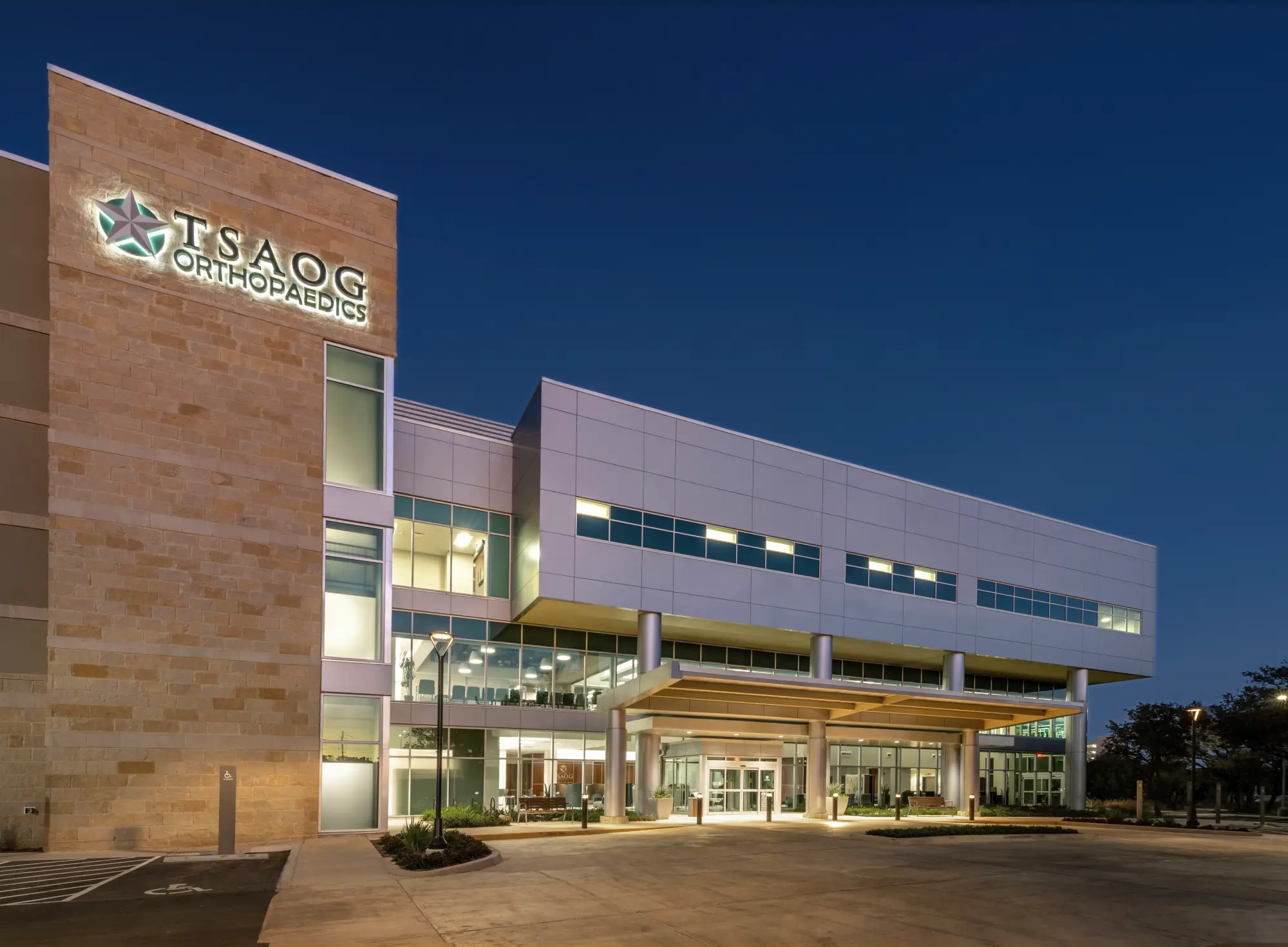 TSAOG Orthopaedics building exterior illuminated at dusk with stone facade tower, modern drop-off canopy, and multi-story glass windows.